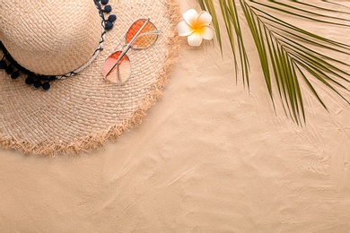 Flat lay composition with stylish hat, flower and tropical leaf on sand