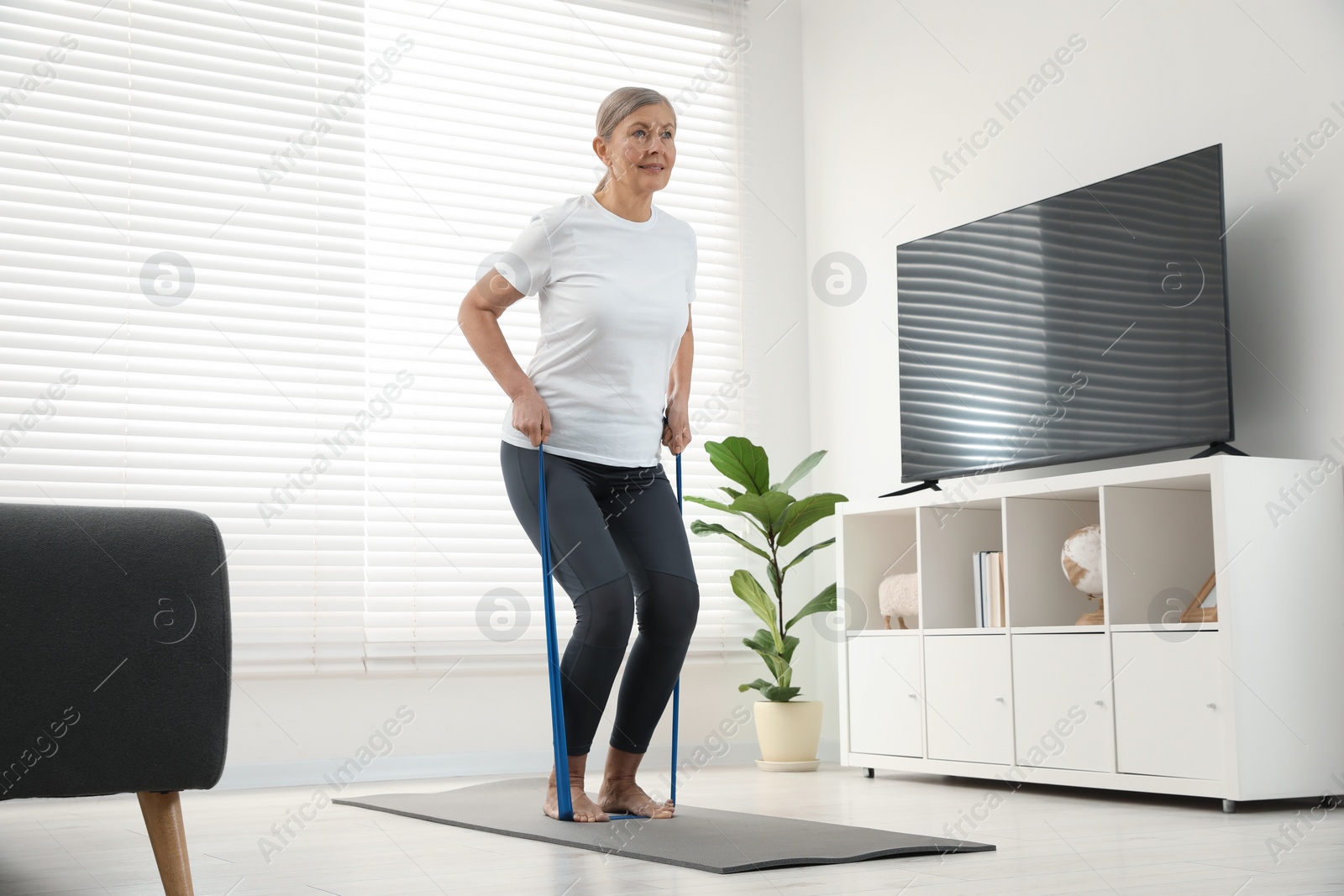 Photo of Senior woman doing exercise with fitness elastic band on mat at home