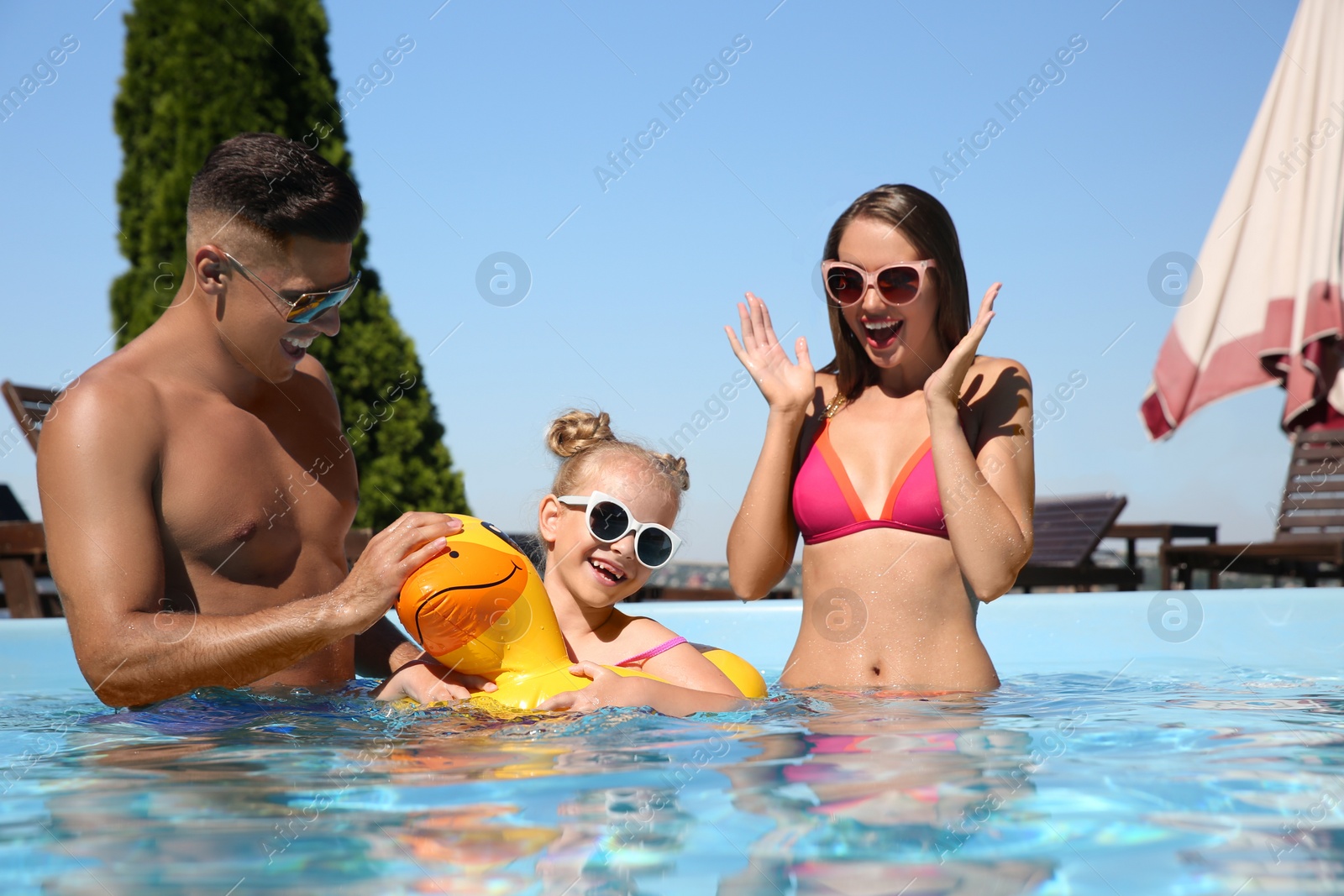 Photo of Happy family with inflatable ring in outdoor swimming pool on sunny summer day