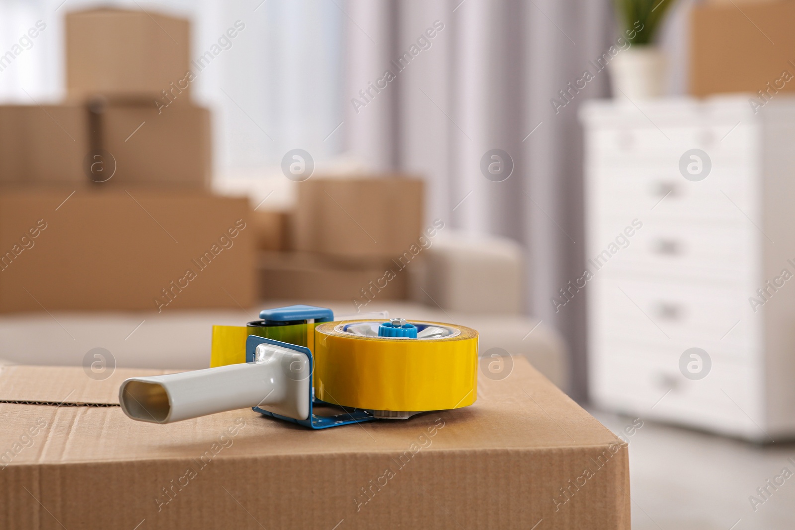 Photo of Dispenser with roll of adhesive tape on box indoors. Space for text
