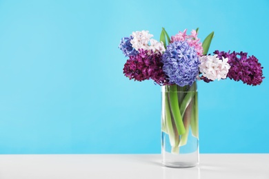 Beautiful hyacinths in glass vase on table against color background, space for text. Spring flowers