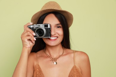 Photo of Beautiful young woman with straw hat and camera on light green background