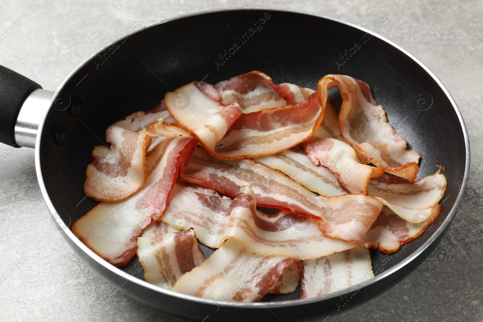 Photo of Delicious bacon slices in frying pan on light grey table, closeup