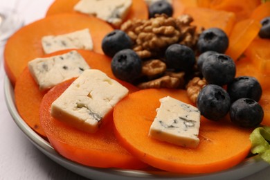 Delicious persimmon with blue cheese, blueberries and walnuts on plate, closeup
