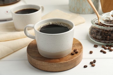 Aromatic coffee in cup and beans on white wooden table