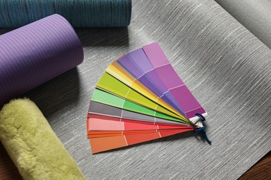 Photo of Different wallpaper rolls, roller and color palette samples on table