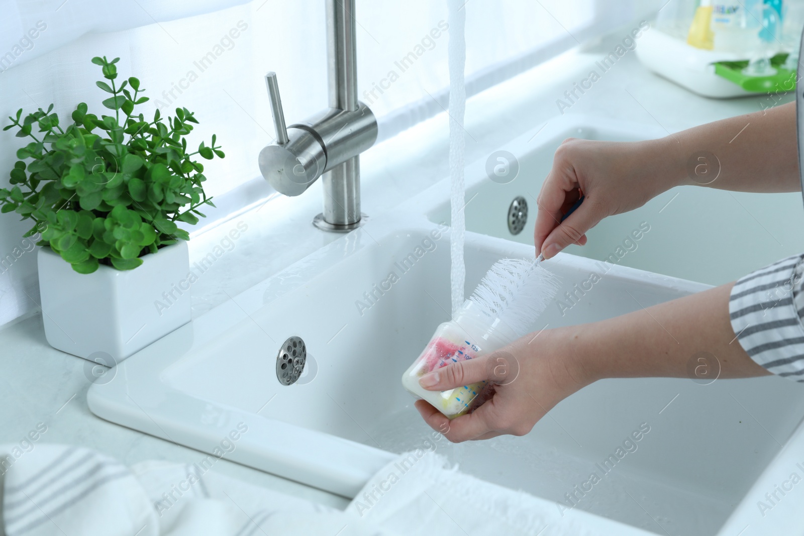 Photo of Woman washing baby bottle in kitchen, closeup