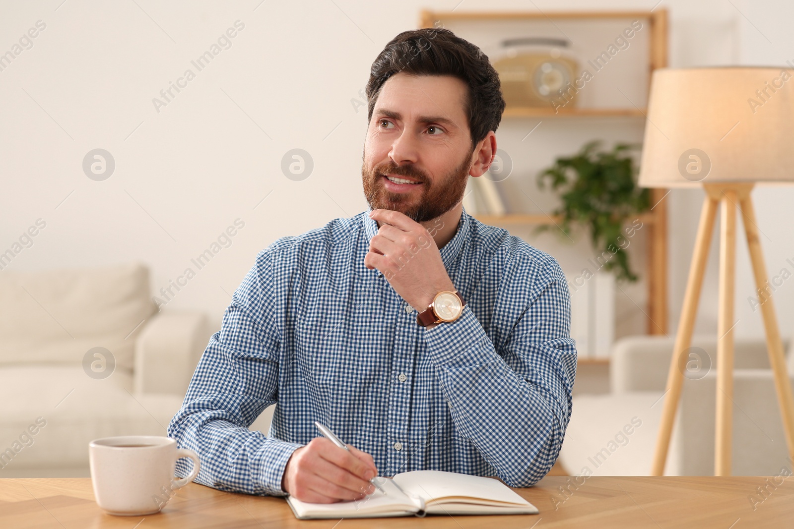 Photo of Happy man taking notes during video call at wooden desk indoors, view from camera