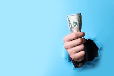 Photo of Businessman breaking through light blue paper with money in fist, closeup. Space for text