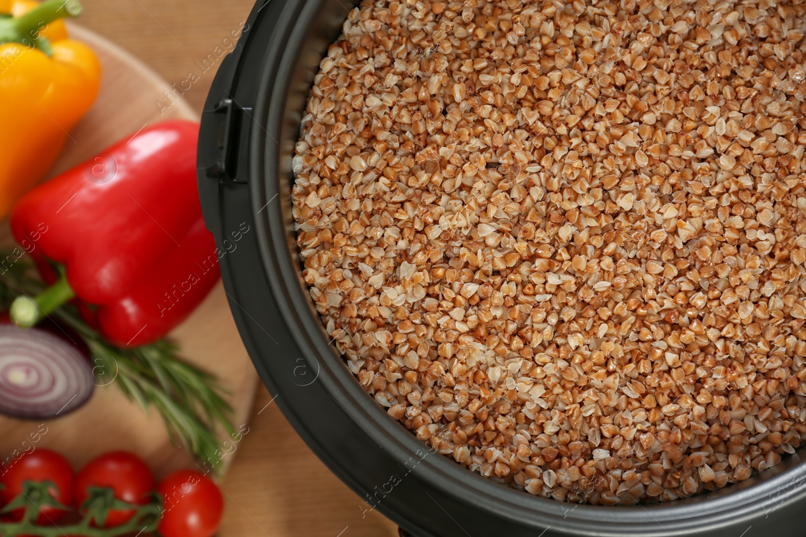 Photo of Delicious buckwheat in multi cooker and vegetables on wooden table, top view