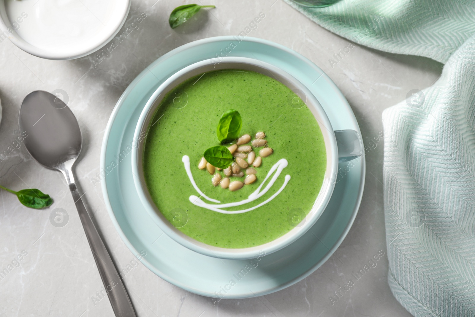 Photo of Cup of healthy green soup with fresh spinach served on light table, flat lay