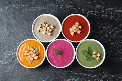 Different tasty cream soups in bowls on black textured table, flat lay