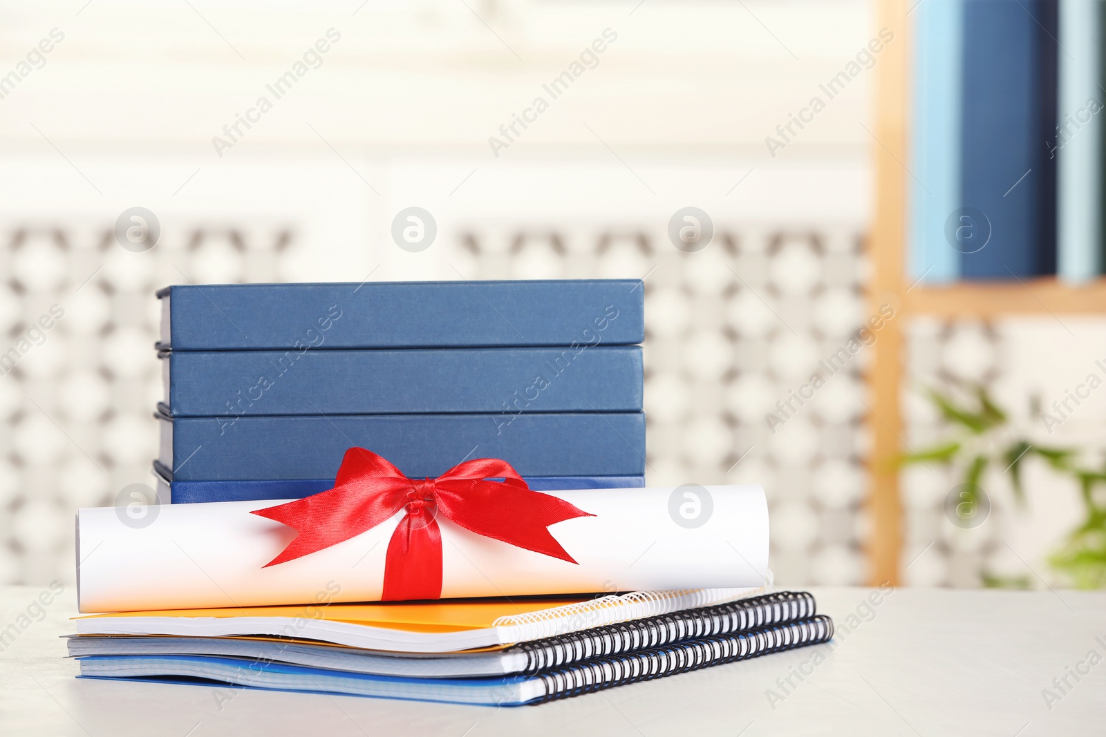 Photo of Graduate diploma with books and notebooks on table against blurred background