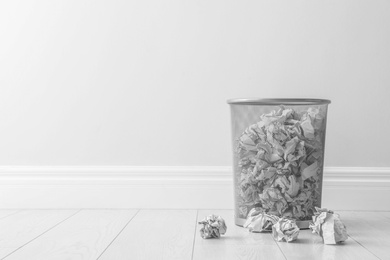 Metal bin and crumpled paper against light wall, space for text