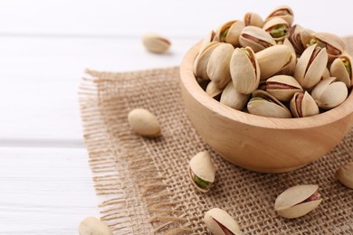 Photo of Tasty pistachios in bowl on white wooden table, closeup. Space for text