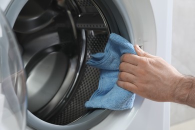 Photo of Man cleaning empty washing machine with rag, closeup