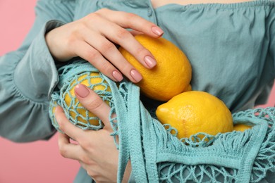 Woman with string bag of fresh lemons on pink background, closeup