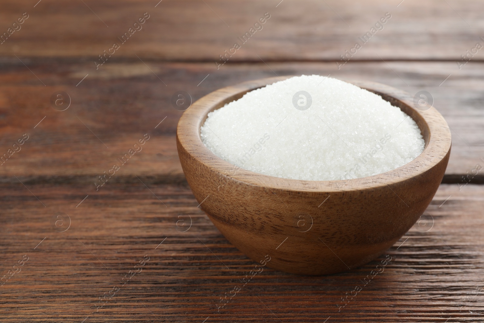 Photo of Granulated sugar in bowl on wooden table, closeup. Space for text