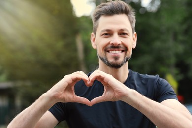 Happy man making heart with hands outdoors