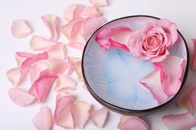 Photo of Bowl with water and rose petals on white background, closeup. Spa composition