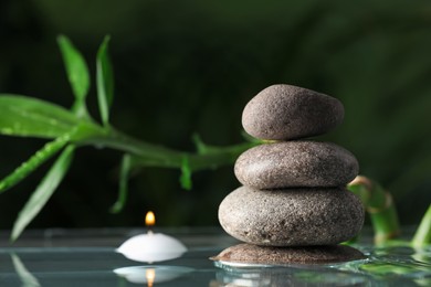 Stacked stones and burning candle with bamboo stem on water surface against dark background, closeup