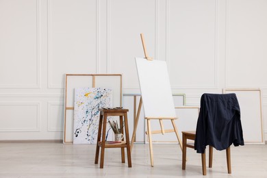 Photo of Wooden easel with canvas, chair and painting supplies in artist's studio