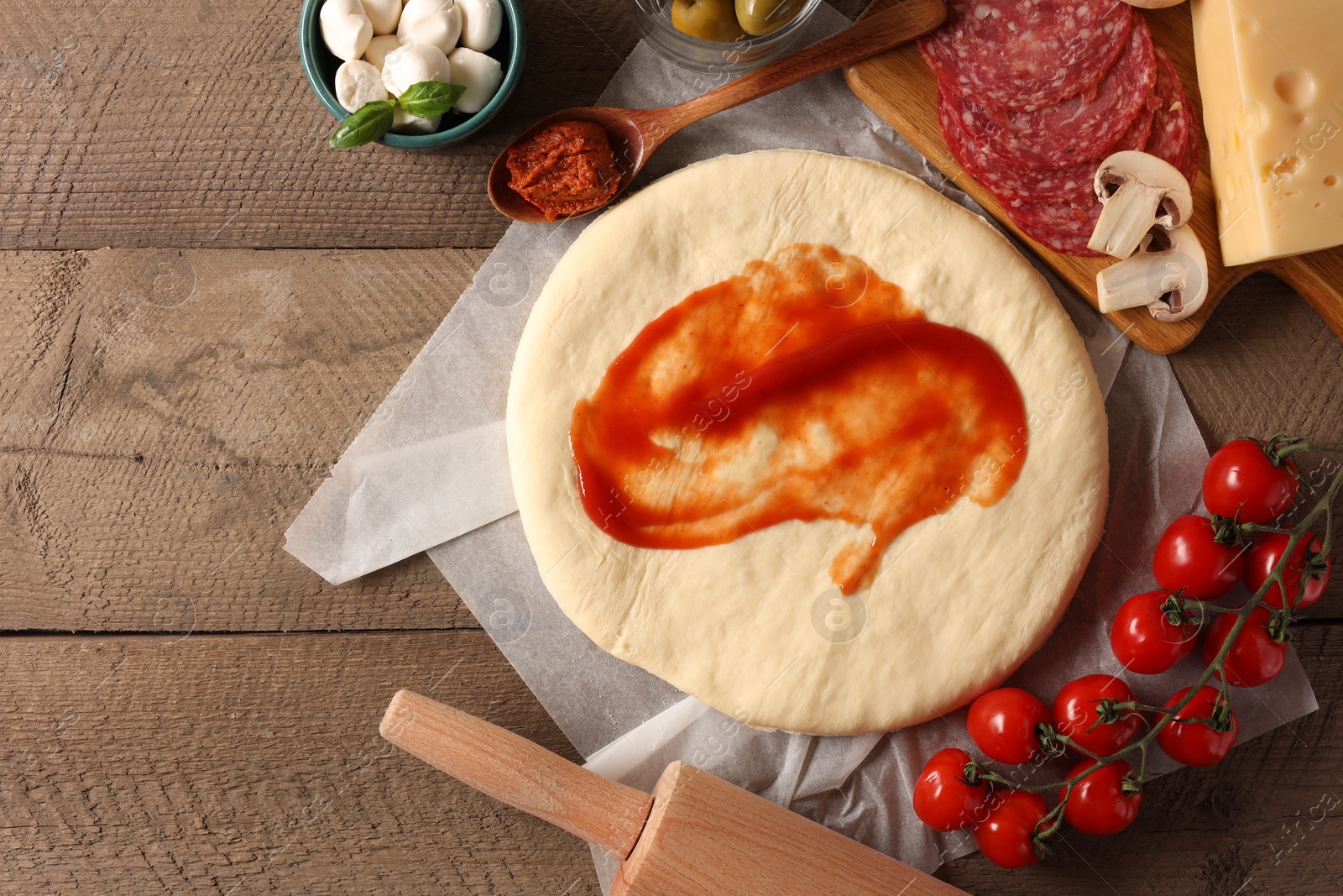 Photo of Pizza dough with tomato sauce, products and rolling pin on wooden table, flat lay. Space for text