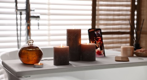 Photo of White wooden tray with burning candles on bathtub in bathroom