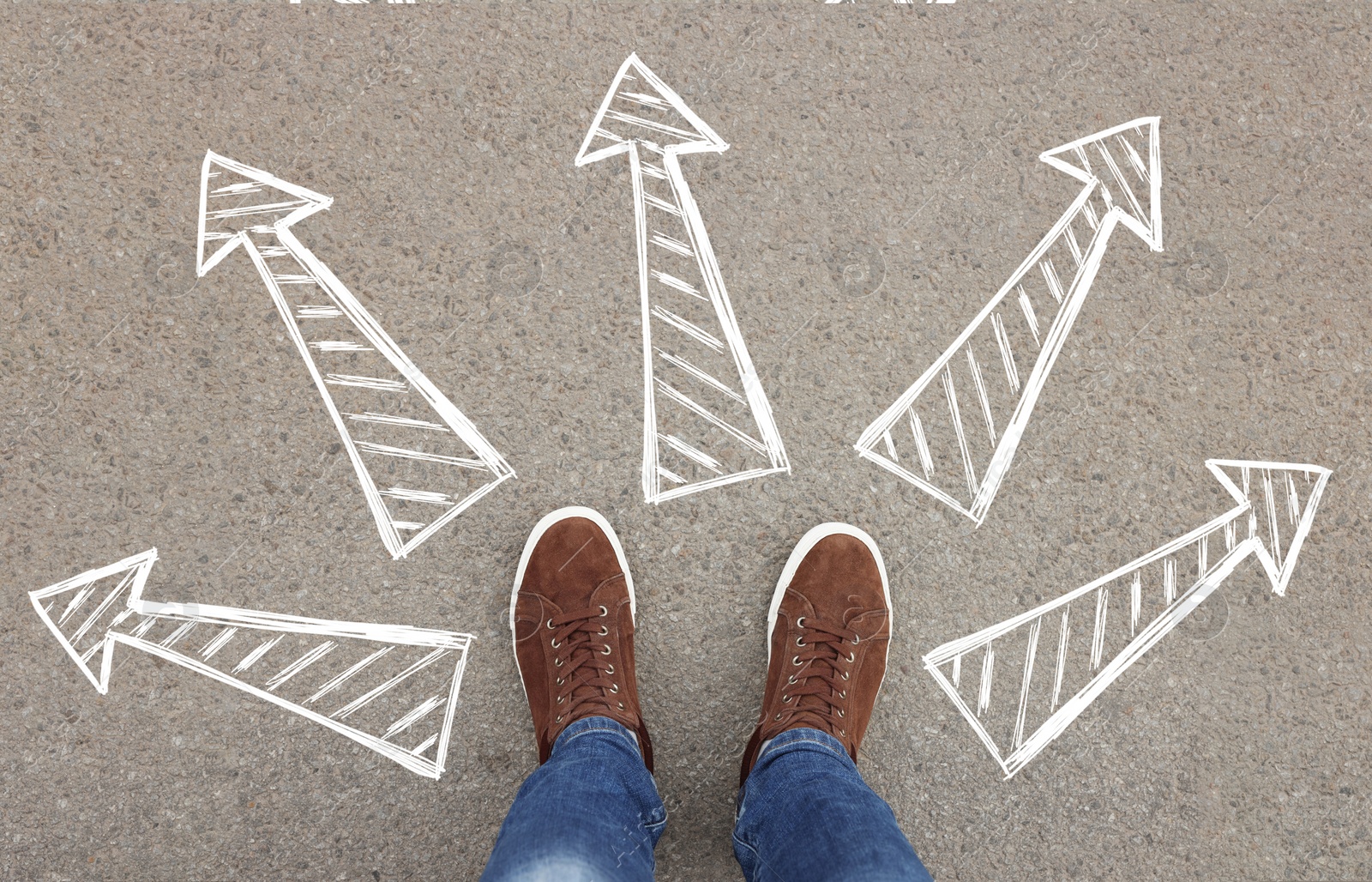 Image of Choosing future profession. Man standing in front of drawn signs on asphalt, top view. Arrows pointing in different directions symbolizing diversity of opportunities