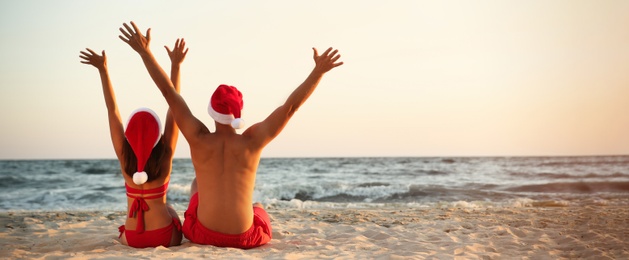 Lovely couple in Santa hats together on beach, banner design. Christmas vacation