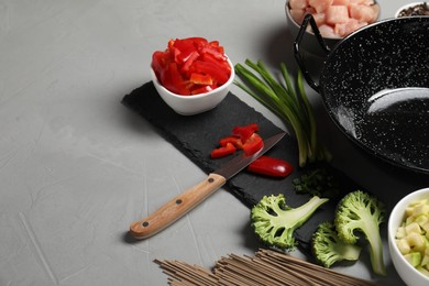 Photo of Wok pan, noodles, chicken and other products on light grey table. Space for text