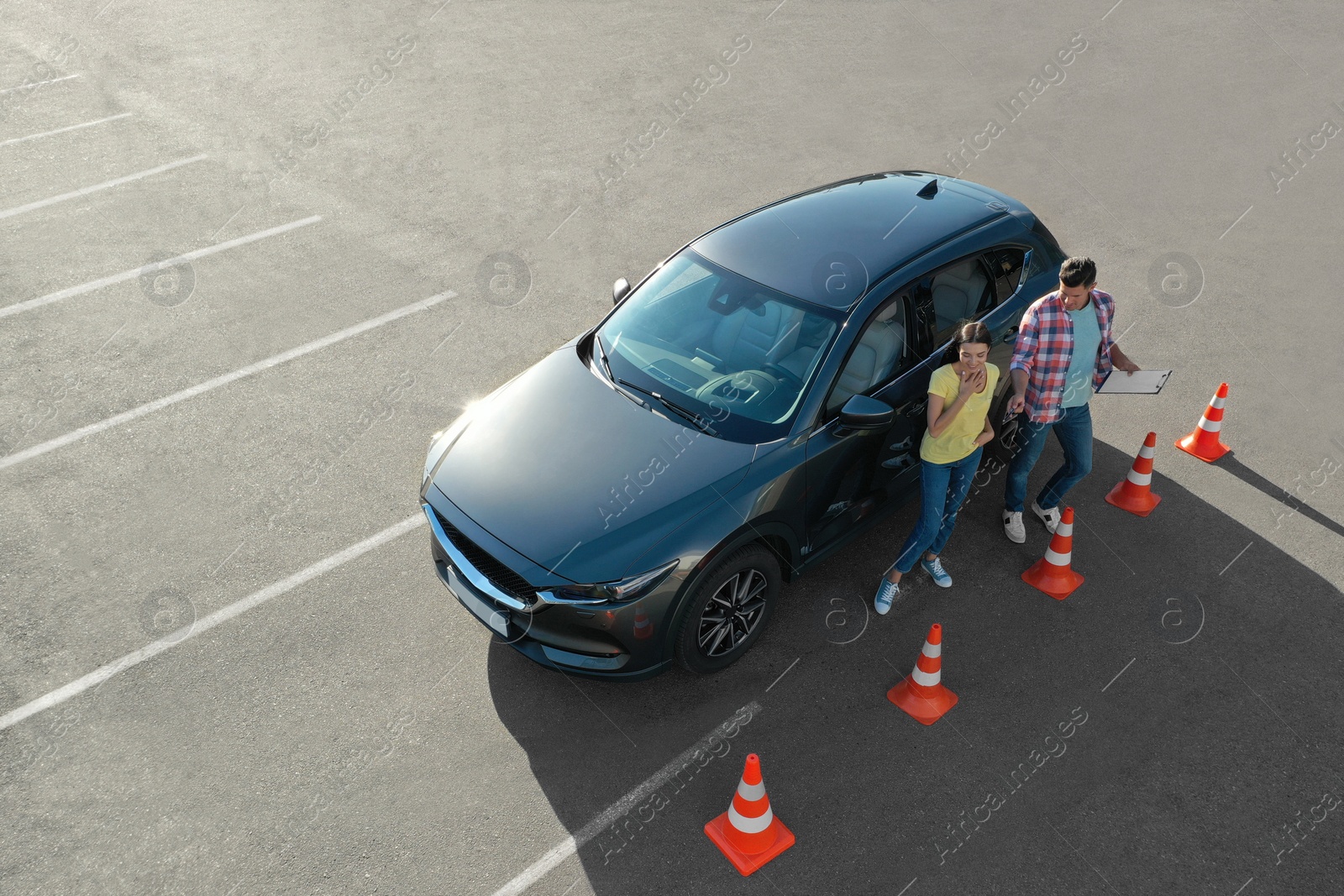 Photo of Instructor with clipboard near car and his student outdoors, above view. Driving school exam