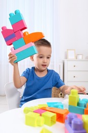Photo of Cute little boy playing with colorful building blocks at table in room