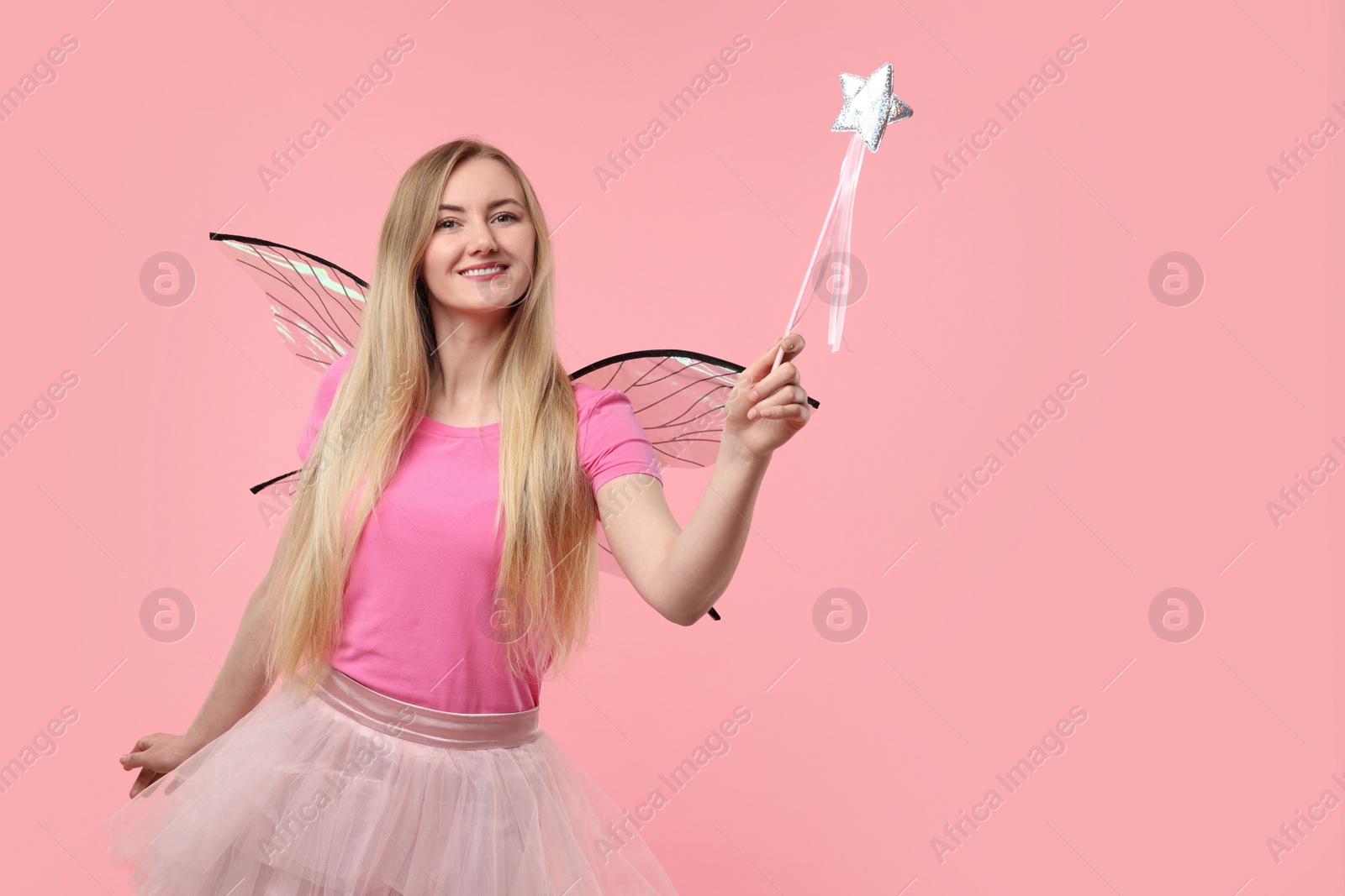 Photo of Beautiful girl in fairy costume with wings and magic wand on pink background, space for text