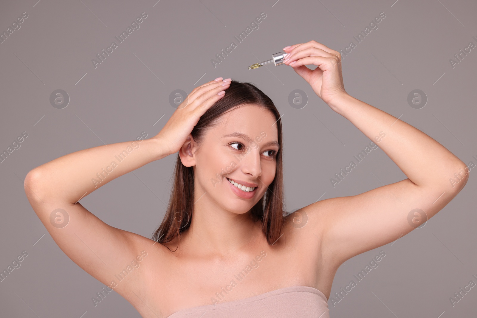 Photo of Beautiful woman applying serum onto hair on grey background