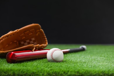 Photo of Baseball bat, leather glove and ball on green grass against dark background. Space for text