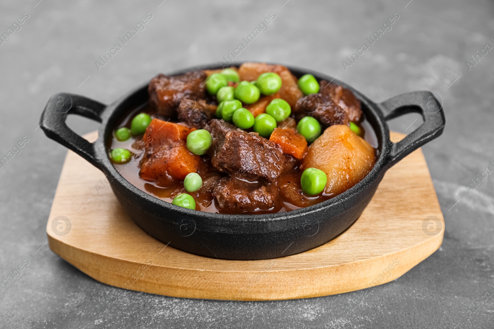 Photo of Delicious beef stew with carrots, peas and potatoes on grey table, closeup