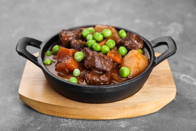Delicious beef stew with carrots, peas and potatoes on grey table, closeup