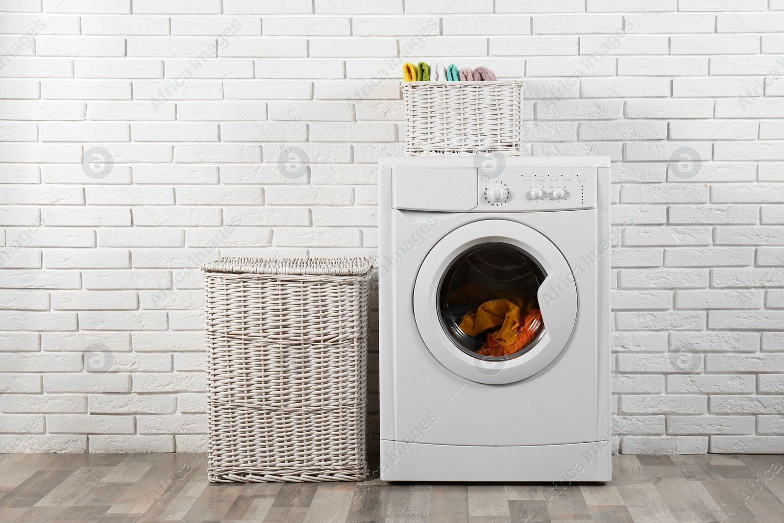 Photo of Modern washing machine and laundry baskets near white brick wall