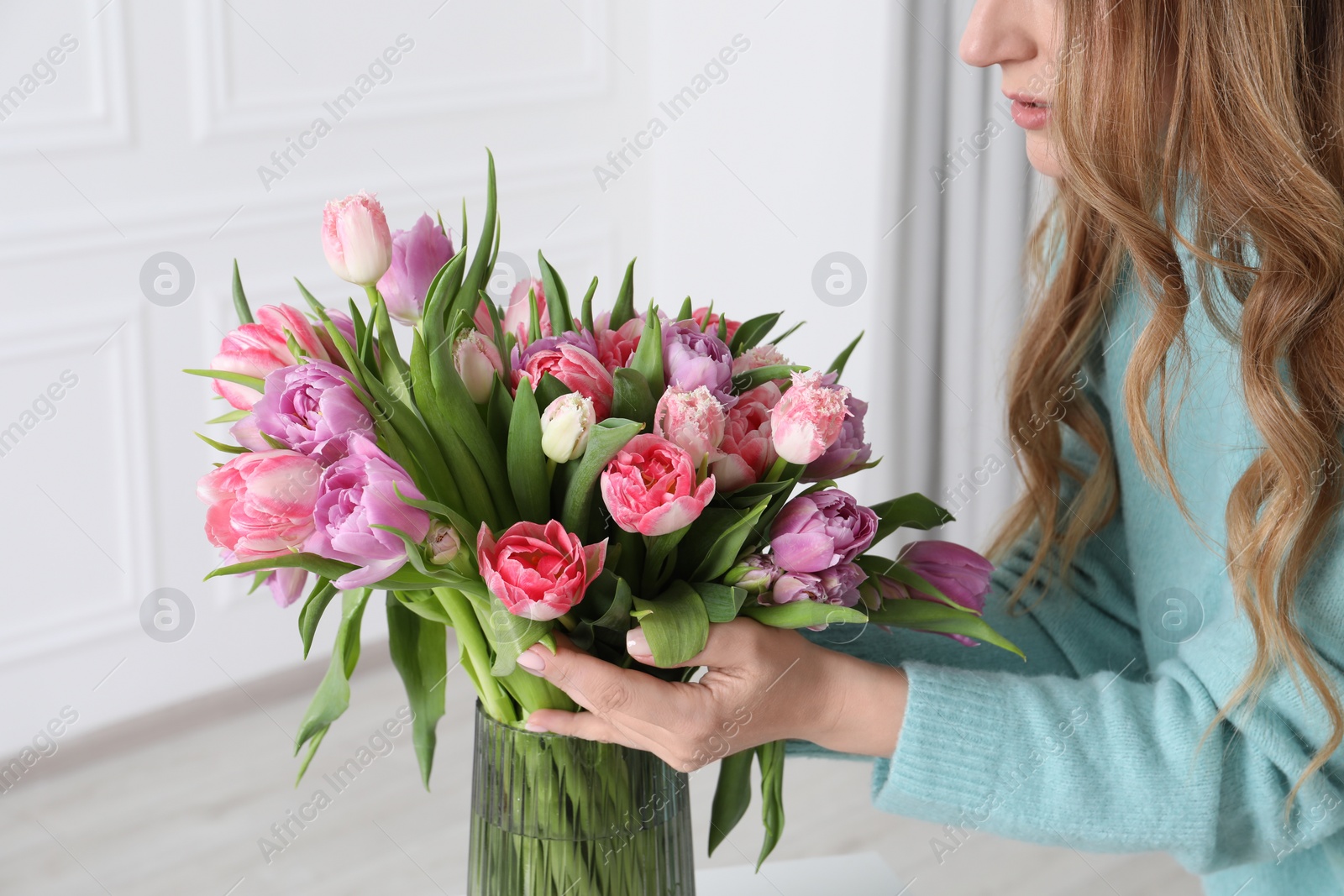 Photo of Woman putting bouquet of beautiful tulips in vase indoors, closeup