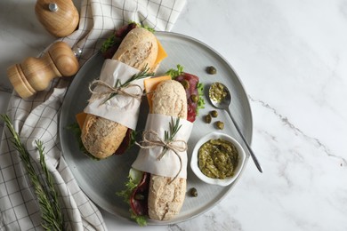 Photo of Delicious sandwiches with bresaola, cheese and lettuce served on white marble table, flat lay. Space for text
