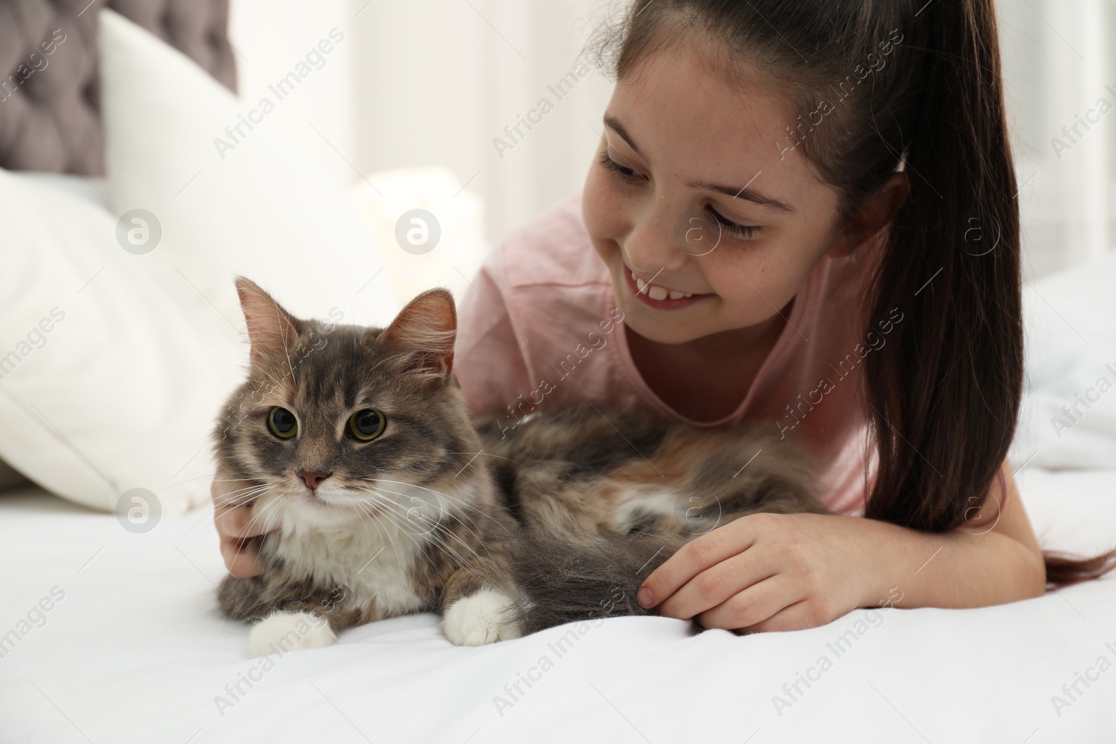 Photo of Cute little girl with cat lying on bed at home. First pet