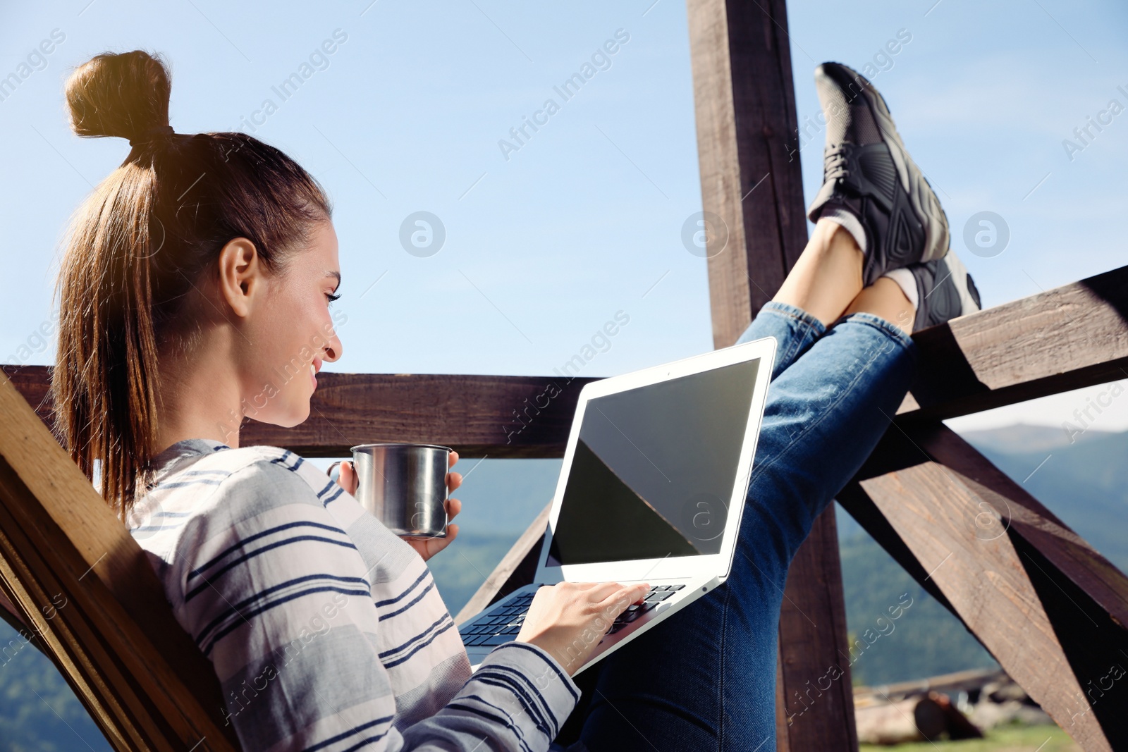 Photo of Young woman working with laptop on outdoor wooden terrace in mountains