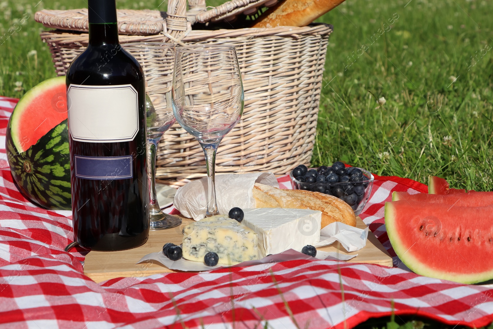 Photo of Picnic blanket with delicious food and wine outdoors on summer day