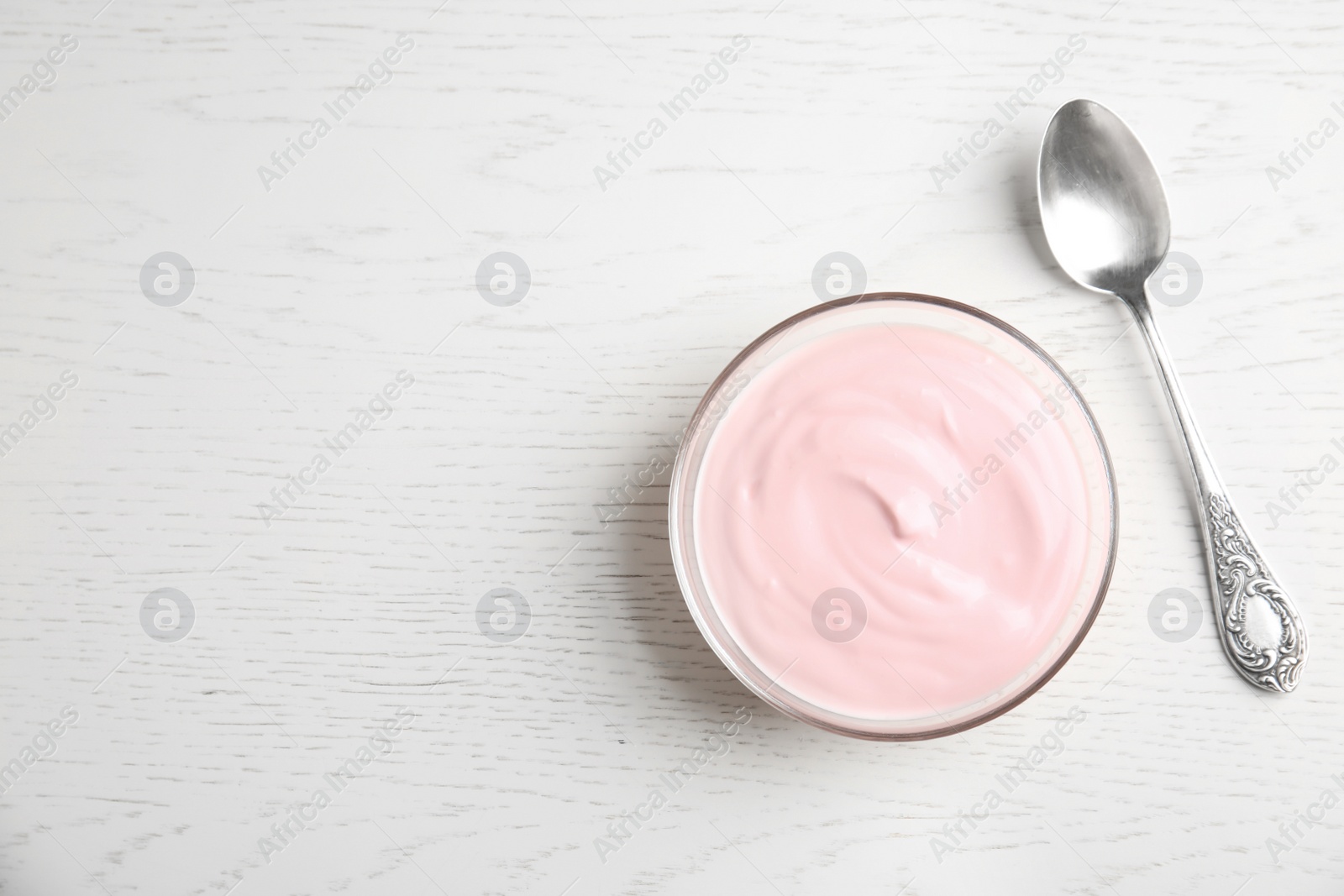 Photo of Glass bowl with creamy yogurt, spoon and space for text on white wooden background, top view