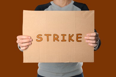 Image of Woman holding Strike sign on dark orange background, closeup