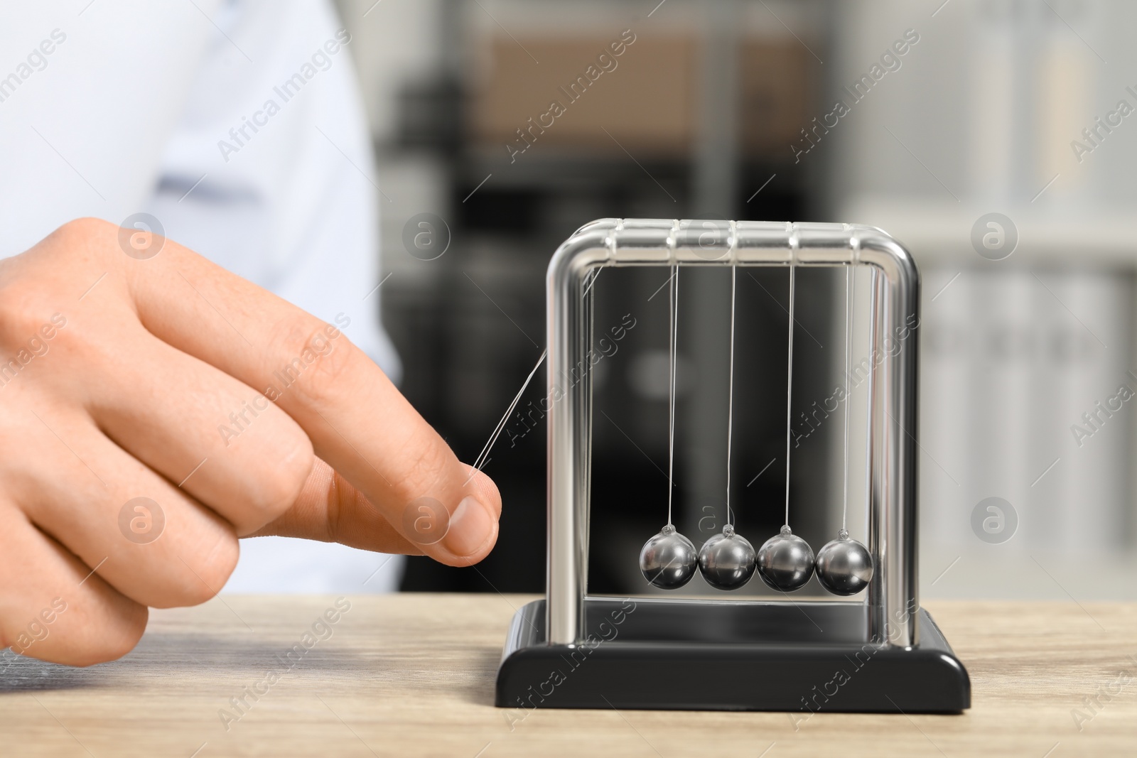 Photo of Man playing with Newton's cradle at wooden table, closeup. Physics law of energy conservation