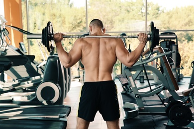 Strong young man lifting barbell in gym