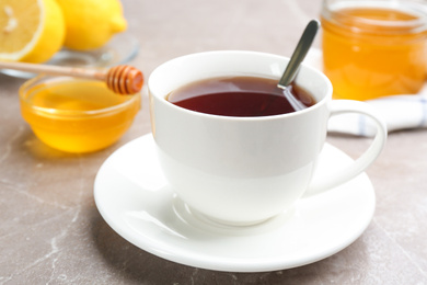 Photo of Cup of tea and tasty honey on brown marble table, closeup