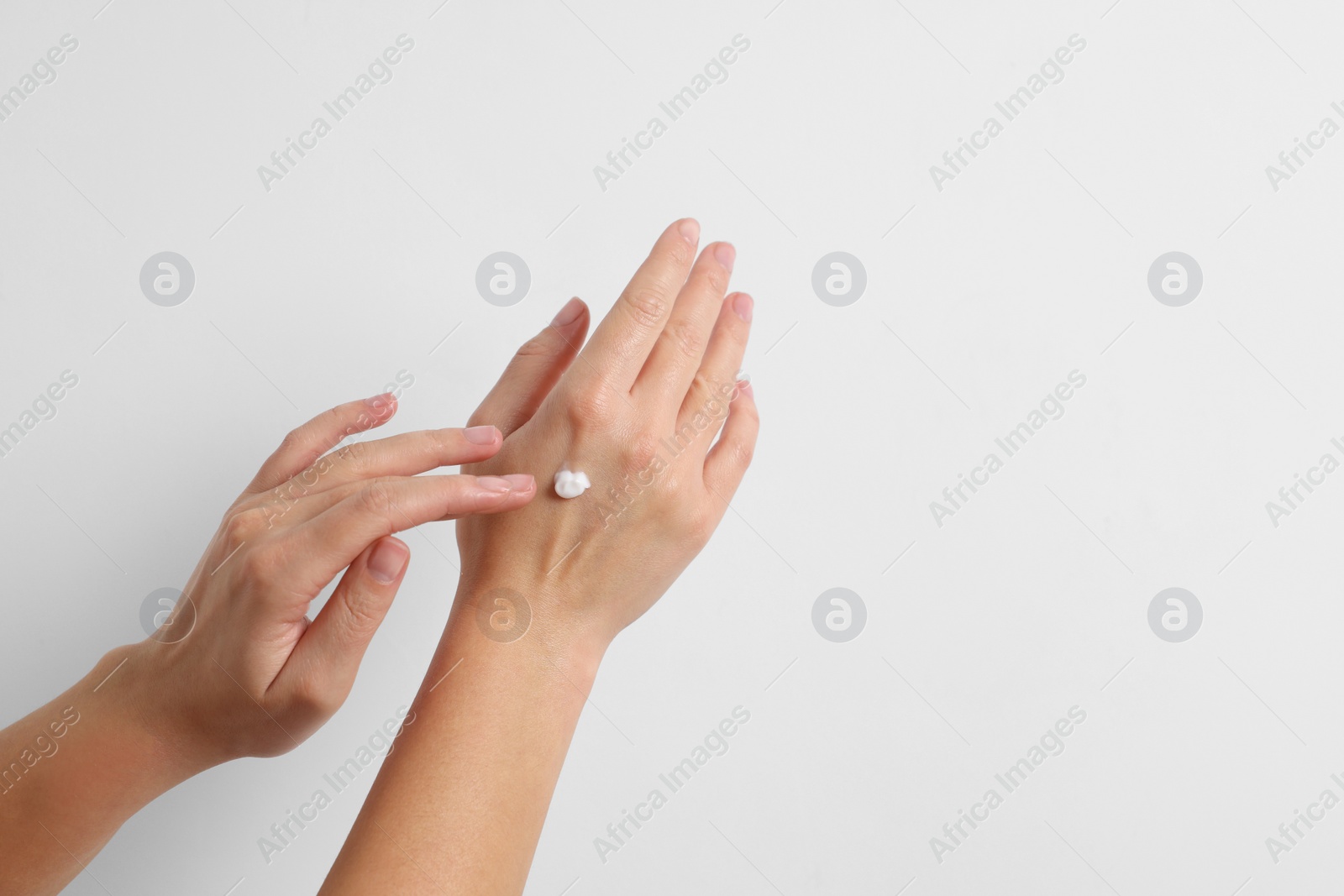 Photo of Woman applying cosmetic cream onto hand on white background, closeup. Space for text